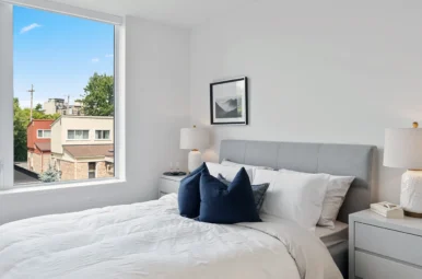 A cozy bedroom with a big window and a white bed, perfect for a peaceful night's sleep after interior painting.